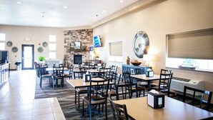 A spacious dining area with multiple tables and chairs, a stone accent wall, a television, and a fireplace. - Cobblestone Inn & Suites - Clarinda (Clarinda)