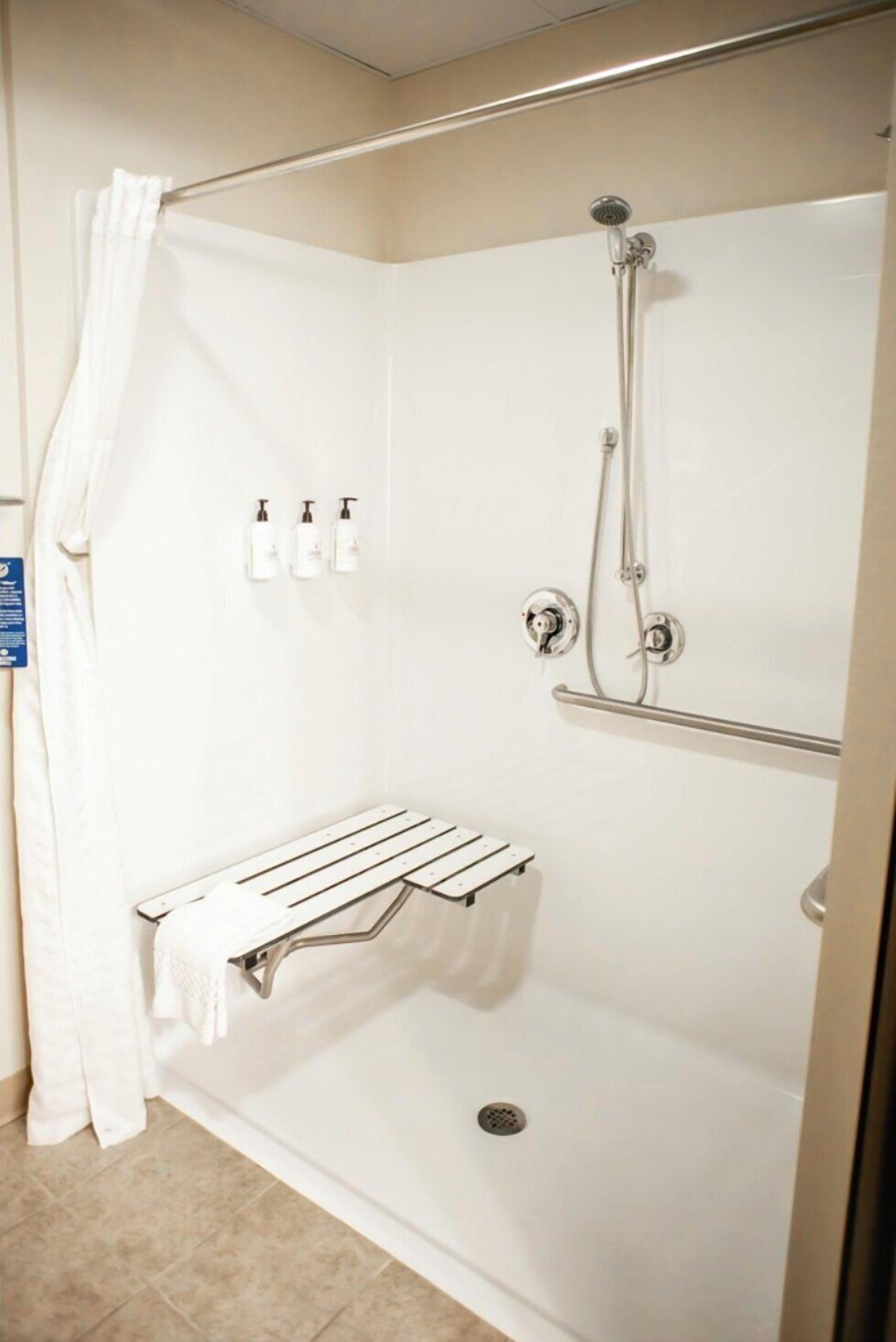 Une douche à l’italienne avec un rideau blanc, un porte-serviettes et deux bouteilles de shampoing.
