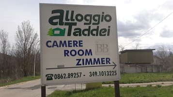 Placa para 'Alloggio Taddei' com números de contato e indicação para 'CAMERE ROOM ZIMMER'.