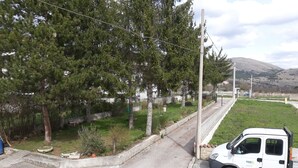 Una camioneta blanca estacionada en una calle con acera, árboles y un área verde al fondo.