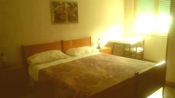 Uma cama de solteiro com cabeceira de madeira, uma mesa de cabeceira com abajur e uma cadeira.
