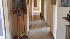 Un pasillo con suelo de terrazo, obras de arte enmarcadas en las paredes y una puerta al final.