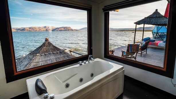 A bathroom with a large bathtub and two windows offering views of a dock and water. - Uros LodgeTiticaca Peru (Puno)
