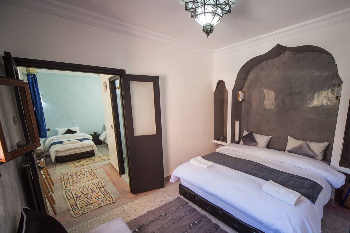 A hotel room with a large bed, a wardrobe, a mirror, and a door leading to another room.