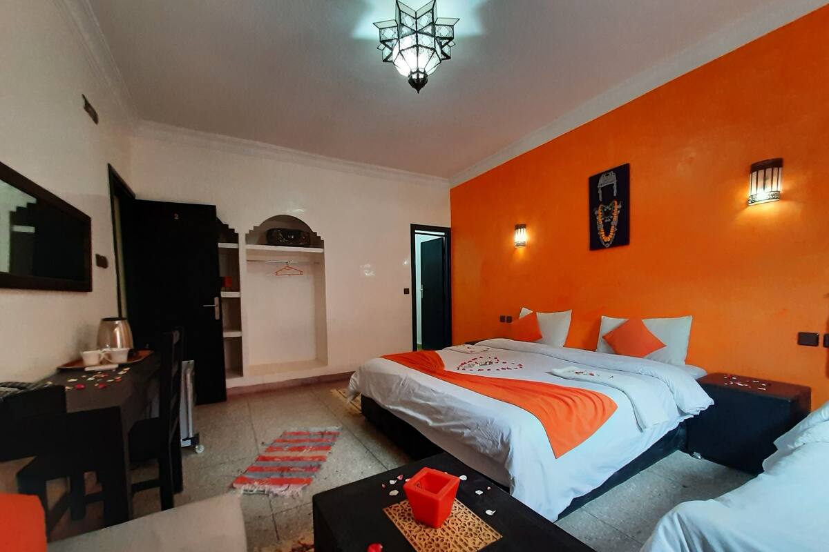 A hotel room with a bed, a desk, a chair, and a small table with a decorative item.