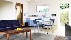 A compact living space with a sofa, dining table, chairs, a small kitchen area, and a TV. - Martinborough Motel (Martinborough)