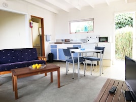 Un espacio habitable compacto con sofá, mesa de comedor, sillas, una pequeña cocina y un televisor.