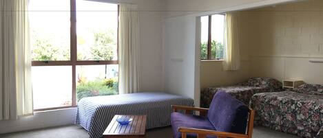 A room with a bed, a chair, a small table, and two windows.