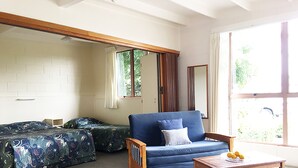 A room with a blue sofa, a wooden table with fruit, and a bed with floral bedding. - Martinborough Motel (Martinborough)
