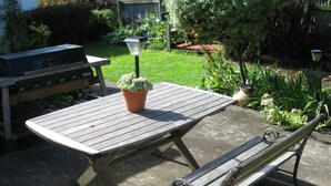 A wooden picnic table with a bench, a potted plant, and a garden in the background. - Martinborough Motel (Martinborough)