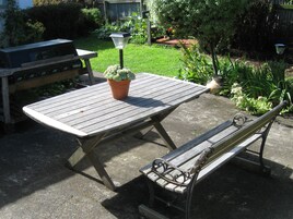 Una mesa de picnic de madera con un banco, una planta en maceta y un jardín al fondo.
