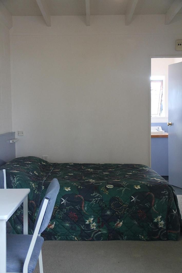 A small, sparsely furnished room with a single bed, a desk, and a chair.