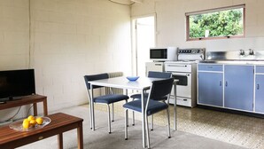 A compact kitchen with white and blue cabinets, a microwave, an oven, and a small dining area with a table and chairs. - Martinborough Motel (Martinborough)