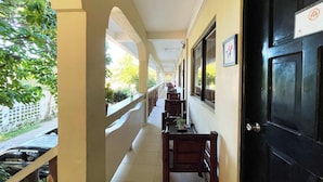 A corridor with a tiled floor, wooden chairs, and a black door with a sign. - Stardust Beach Hotel Matabungkay Batangas (Lian)