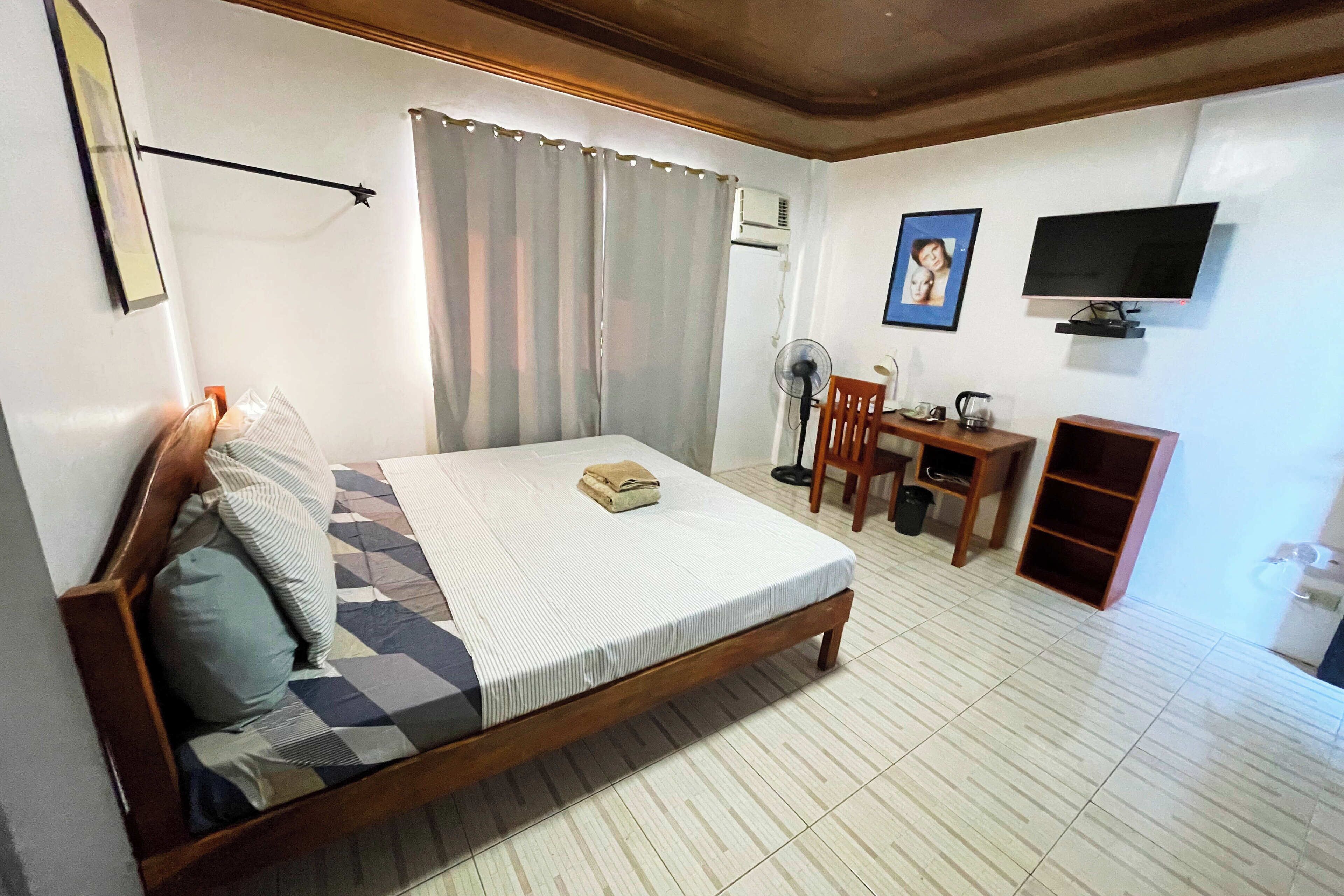 A bedroom with a bed, a desk, a chair, a television, and a wardrobe.