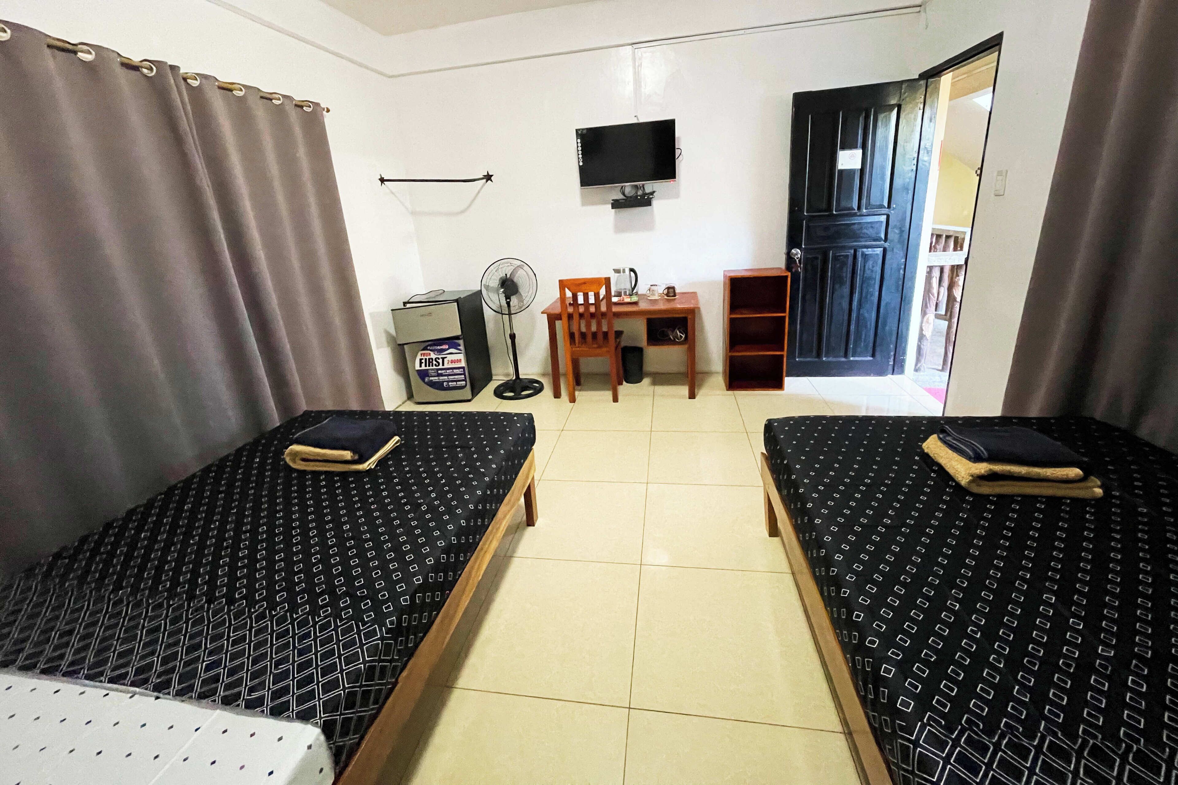 A hotel room with two beds, a desk, a chair, a television, and a door.