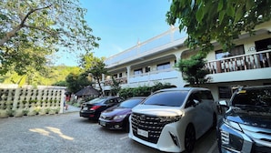 A parking area with several cars, a building with a balcony, and a wall with potted plants. - Stardust Beach Hotel Matabungkay Batangas (Lian)