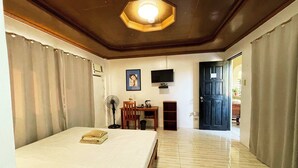 A bedroom with a bed, a desk, a chair, a fan, and a television on the wall. - Stardust Beach Hotel Matabungkay Batangas (Lian)