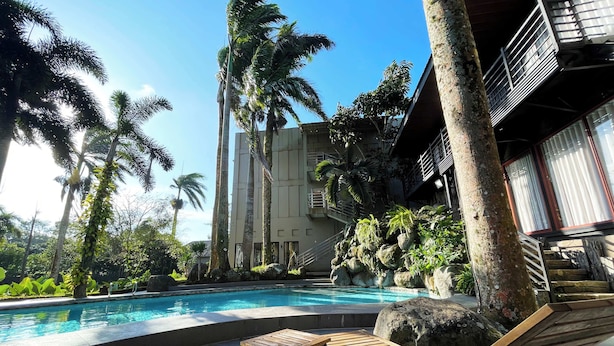 A pool area with lounge chairs and a small table, surrounded by palm trees and a building with balconies. - Stardust Beach Hotel Matabungkay Batangas (Lian)