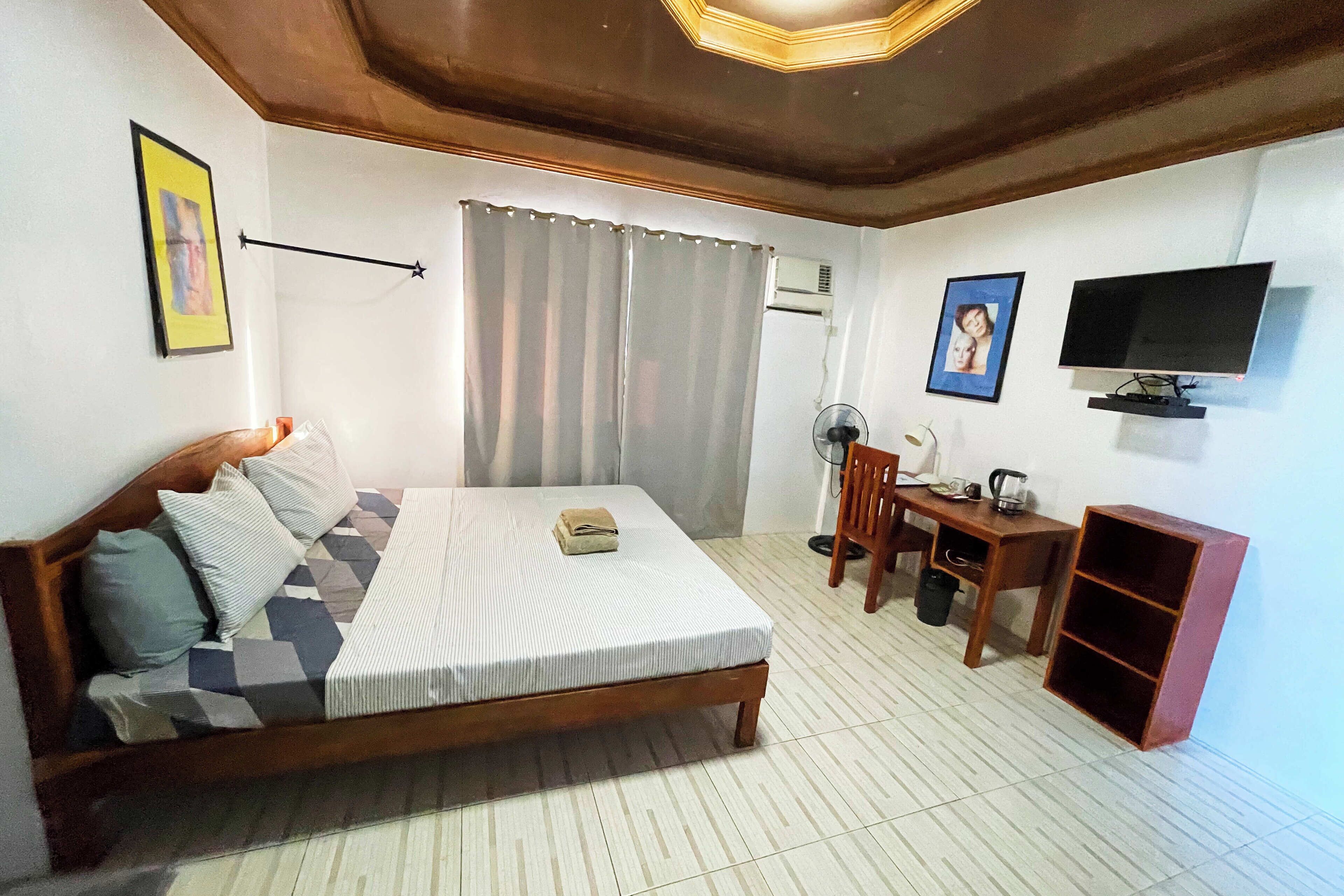 A bedroom with a bed, a desk, a chair, a TV, and a shelf.