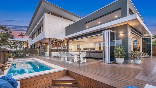 Et moderne hus med swimmingpool, udendørs møbler og en velbelyst patio.