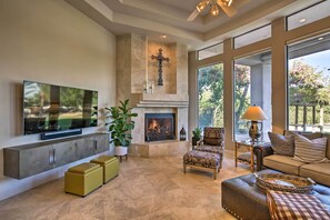 A spacious living room with a fireplace, comfortable seating, a flat-screen TV, and large windows offering a view of the outdoors. - Lavish Paradise Valley Home w/ Sports Court & Pool (Paradise Valley)