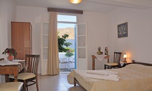 A hotel room with a bed, a table with chairs, a wooden cabinet, a balcony with a view of the sea, and a lamp on the bedside table. - Filoxenia (Amorgos)
