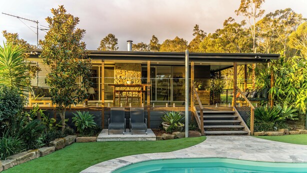 Een modern huis met een zwembad, een overdekt terras en een trap naar een terras.