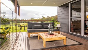 Een balkon met een houten vloer, een grijze bank, een houten salontafel en een glazen balustrade.