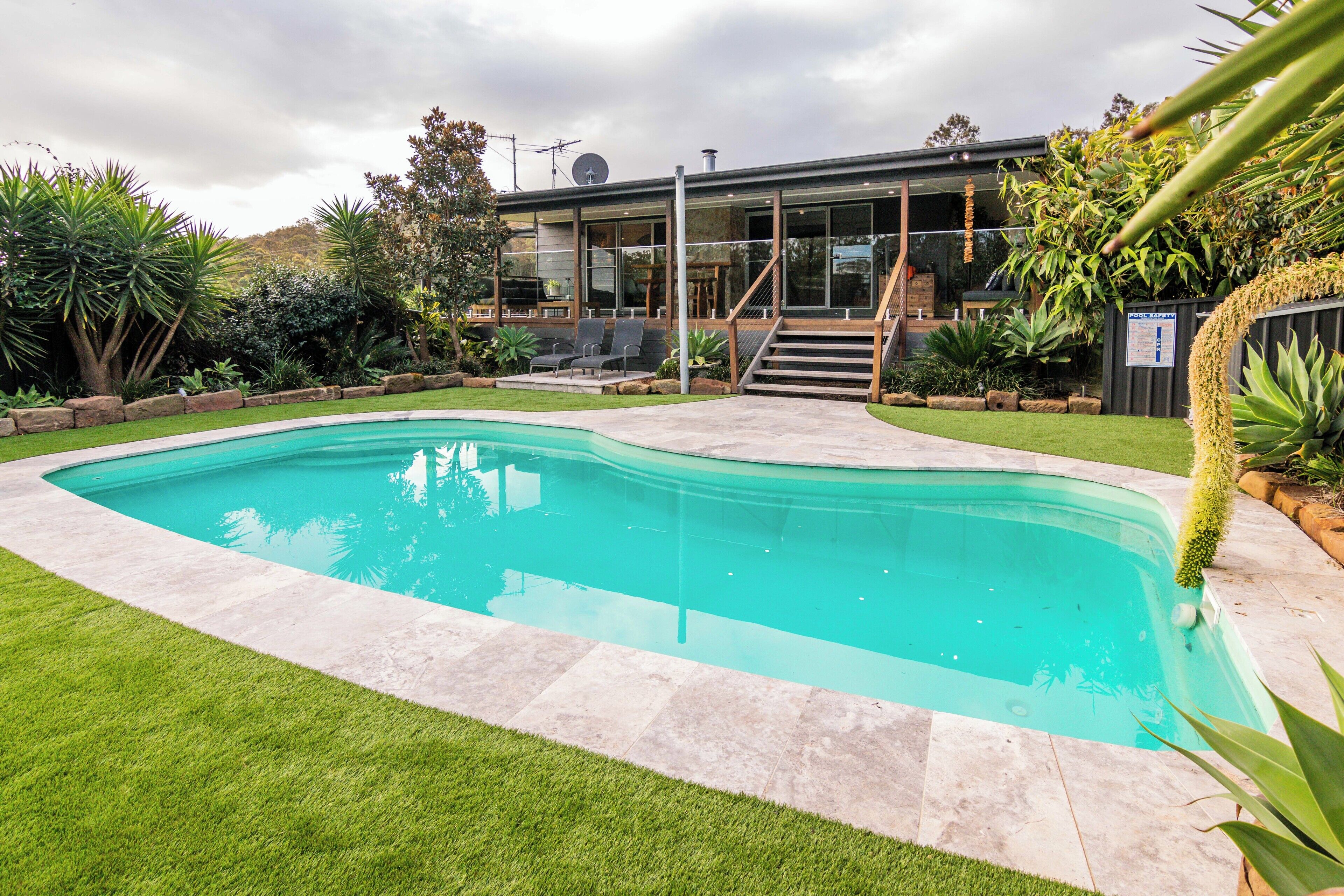 A modern house with a swimming pool, a staircase leading to a deck, and a well-maintained garden.