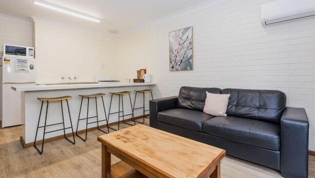 Un espace de vie moderne comprenant un coin cuisine, un canapé en cuir noir et une table basse en bois.
