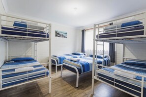 A dormitory room with bunk beds, white brick walls, and a wooden floor.