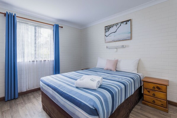 A bedroom with a bed, a wooden nightstand, a window with curtains, and a wall-mounted picture.