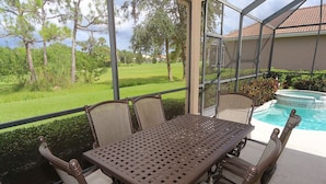 A covered patio with a table and chairs, a pool, and a view of a golf course. - Tailfeather Home on Golf Course by RVA: Stylish 4BR w Pool & Close to Beach (Bradenton)