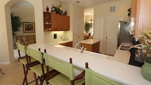 A kitchen with a long island, wooden chairs, and a dining table. - Tailfeather Home on Golf Course by RVA: Stylish 4BR w Pool & Close to Beach (Bradenton)