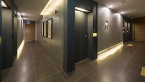A modern hallway with a dark floor, recessed lighting, and a wall-mounted light fixture. - Guseo Browndot Hotel (Busan)