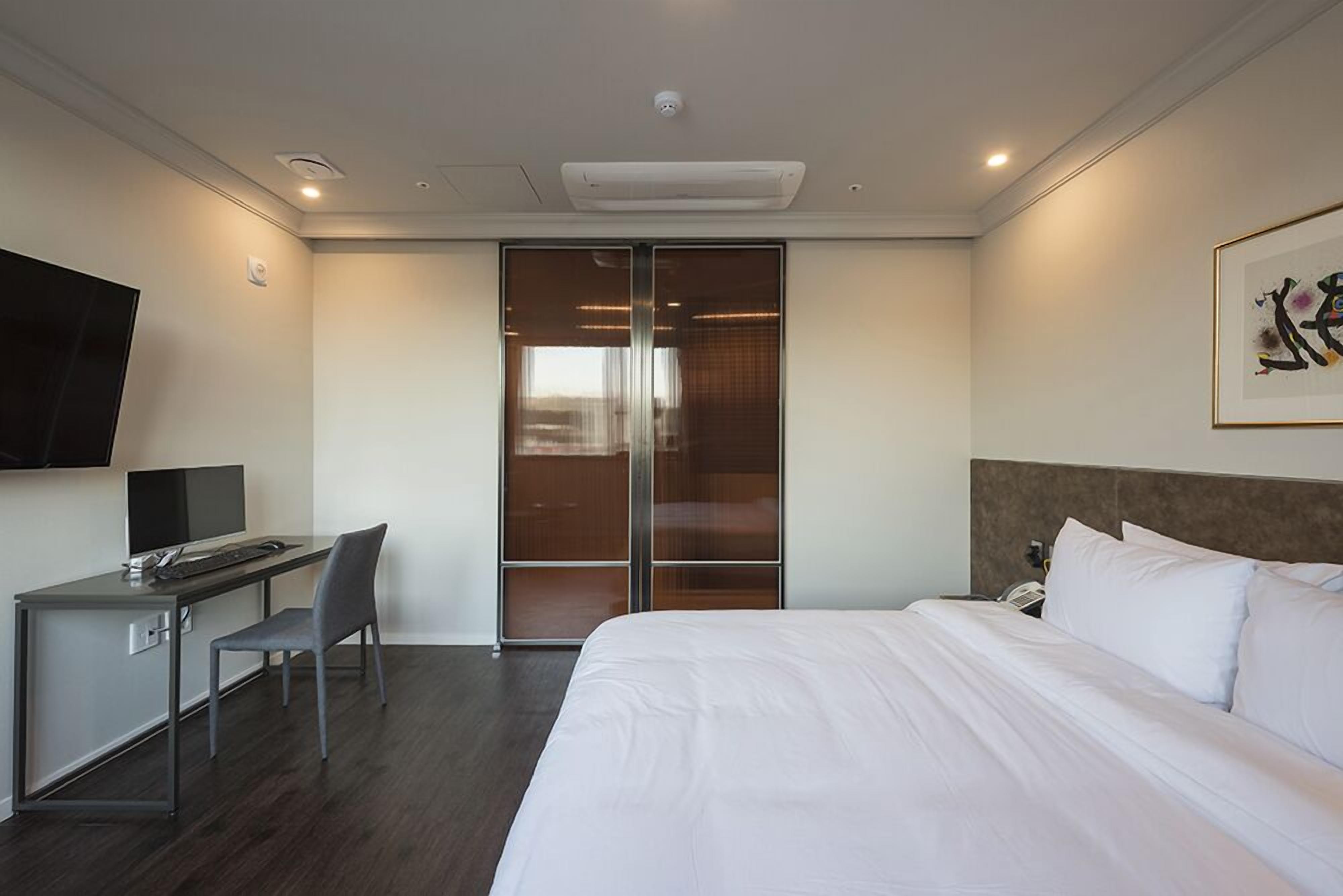 A hotel room with a bed, a desk with a chair, a TV, and a sliding door closet.