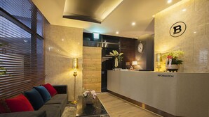 A modern reception area with a reception desk labeled "INFORMATION," a sofa with colorful cushions, a floor lamp, and a clock on the wall. - Guseo Browndot Hotel (Busan)