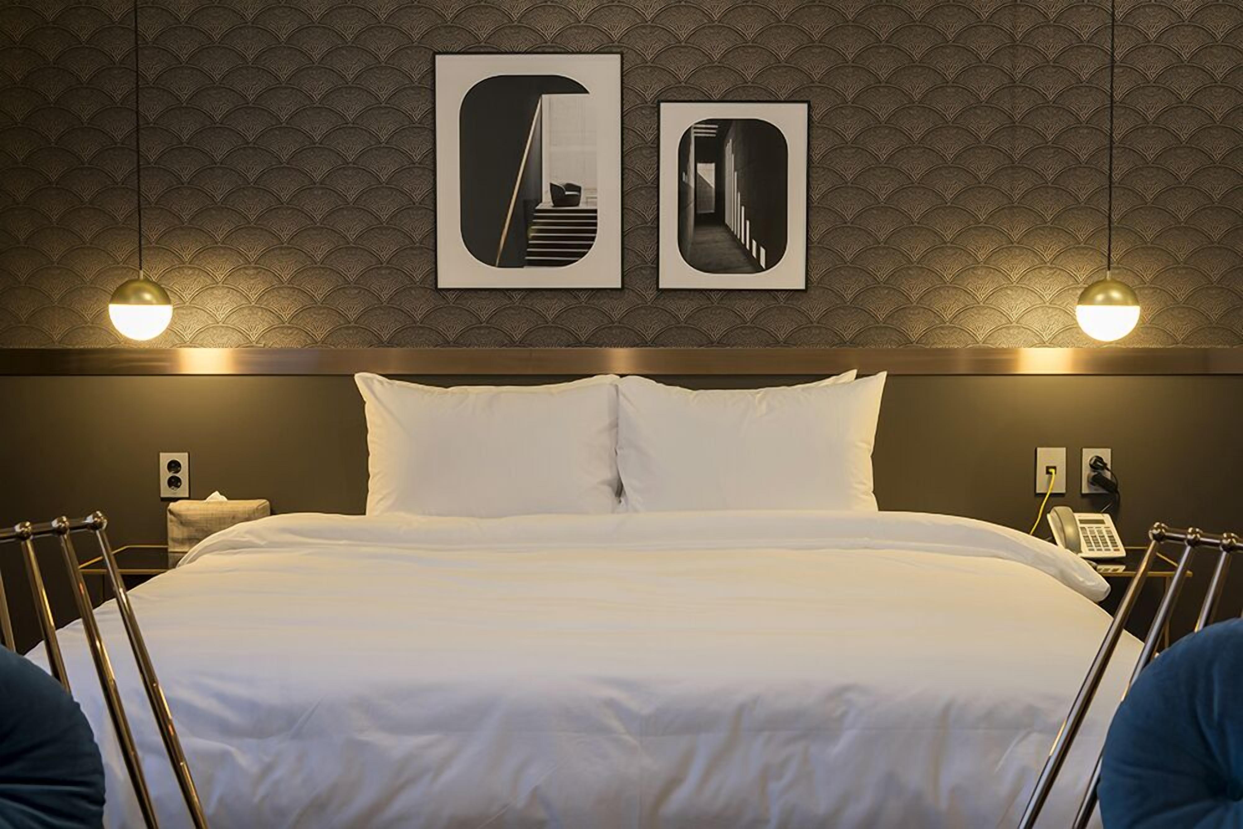 A hotel room with a large bed, two bedside tables, a wall-mounted phone, and two framed pictures above the bed.