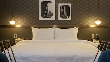 Een hotelkamer met een groot bed, twee nachtkastjes, een aan de muur bevestigd telefoontoestel en twee ingekaderde foto's boven het bed.