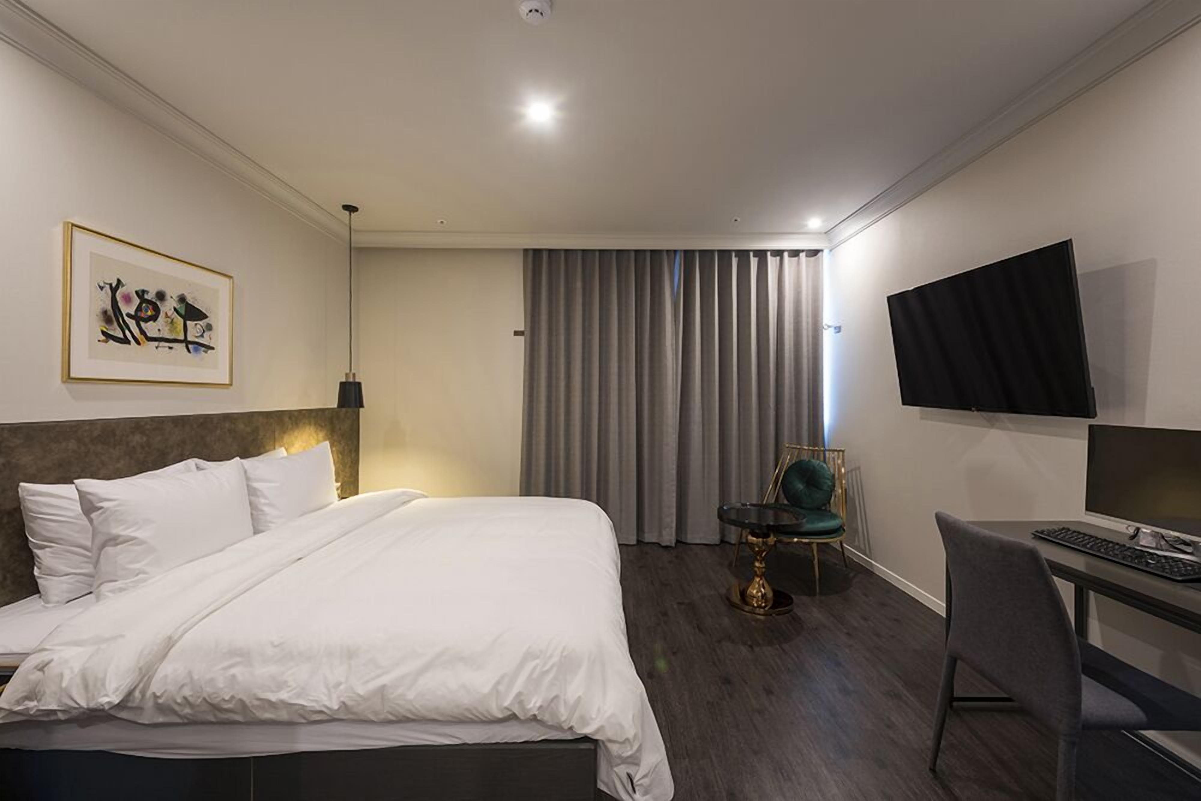 A hotel room with a large bed, a desk with a computer, a chair, a TV, and a painting on the wall.