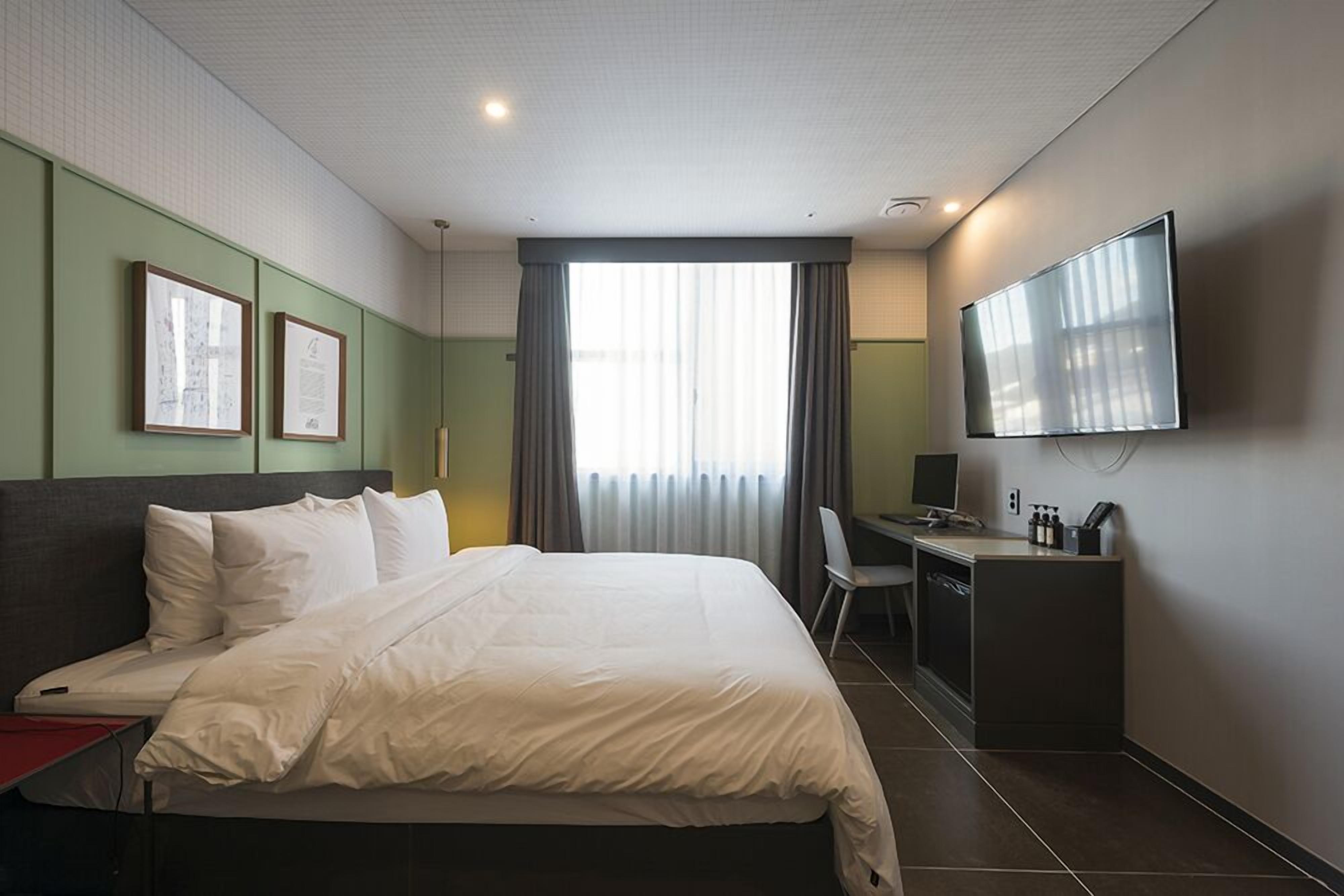 Quarto de hotel com uma cama grande, uma escrivaninha com cadeira, televisão e quadros na parede.