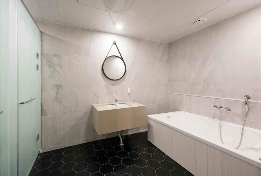 Een badkamer met een witte badkuip, een wastafel met spiegel en zwart mozaïek op de vloer.