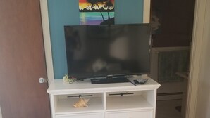 A bedroom with a television on a white dresser, a floral bedspread, and a door leading to another room. - Best Value in Westerly!  (Westerly)