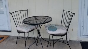 A small outdoor seating area with two metal chairs and a round table, a fire alarm on the wall, and a window with blinds. - Best Value in Westerly!  (Westerly)