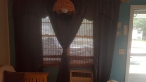 A room with a window covered by a patterned curtain, a wooden chair, and an air conditioning unit. - Best Value in Westerly!  (Westerly)