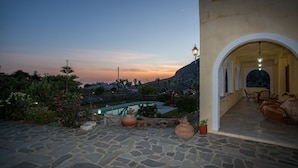 Une terrasse en pierre avec une piscine, un espace salon extérieur et une vue sur une montagne au crépuscule.