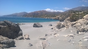 Une plage rocheuse parsemée de gros blocs et offrant une vue dégagée sur la mer et les montagnes lointaines.