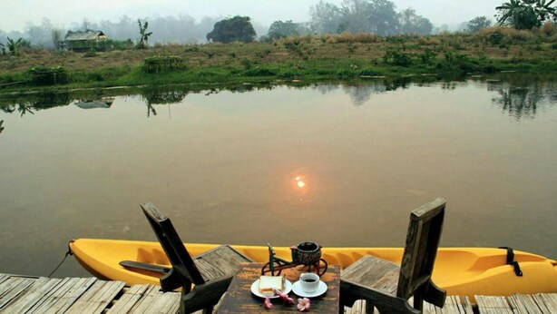 Un muelle de madera con una mesa dispuesta para dos, con vista a una masa de agua tranquila.