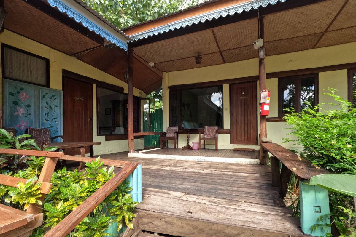 A wooden deck leading to a building with a covered porch, a fire extinguisher, and a window with a view of the outside.